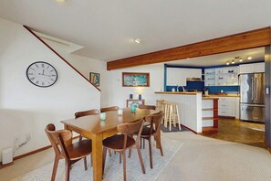 A dining area with a wooden table and chairs, a clock on the wall, and a kitchen with a refrigerator and cabinets. - 3 BR waterfront home with amazing views and beach (Vashon)