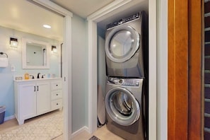 A laundry room with a stacked washer and dryer, a white cabinet with drawers, and a mirror above the sink. - 3 BR waterfront home with amazing views and beach (Vashon)