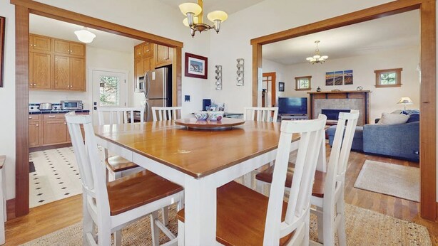 Un comedor con una mesa de madera y sillas blancas, una cocina con armarios de madera, y una sala de estar con un sofá azul y un televisor.
