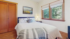 Un dormitorio con cama, mesita de noche, lámpara, ventana con cortinas y armario.