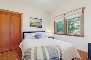 Une chambre à coucher comprenant un lit, une table de chevet, une lampe, une fenêtre avec des rideaux et une armoire.