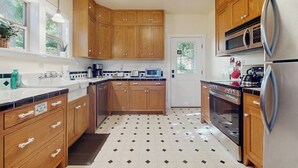 Una cocina con armarios de madera, microondas, refrigerador y piso con baldosas.