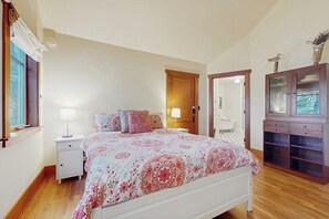 A bedroom with a bed, nightstand, dresser, and a door leading to a bathroom.