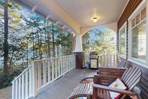 A covered outdoor deck with a view of a forest and a body of water.