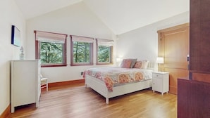 A bedroom with a bed, bedside tables, a dresser, and windows with a view of trees. - 3BR Oceanfront Dog Friendly | Fireplace (Port Townsend)