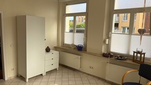 A room with a white wardrobe, a radiator, a window with a view of buildings, and a chair.