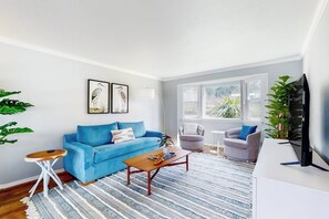 A living room with a blue sofa, a wooden coffee table, and a television on a white stand. - 4BR dog-friendly with water views & deck (Shelton)