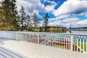 A wooden deck with a white railing overlooking a calm lake, surrounded by trees and a clear sky. - 4BR dog-friendly with water views & deck (Shelton)