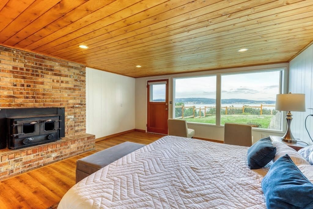 Ein Schlafzimmer mit einem großen Bett, einem Kamin, Blick durch ein Fenster und einer Tür zum Ausgang.