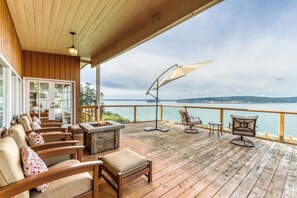 Eine Holzterrasse mit Sitzgelegenheiten im Freien, einer Feuerstelle und Blick auf einen See.