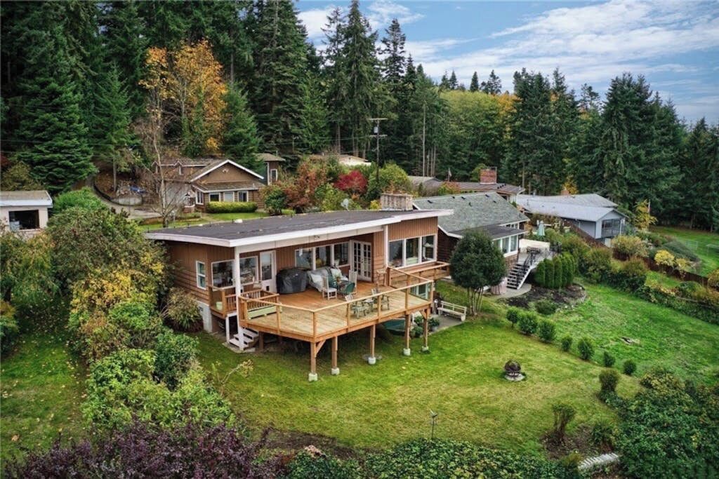 Ein zweistöckiges Haus mit einer Terrasse, umgeben von dichtem Wald und einem gepflegten Rasen.