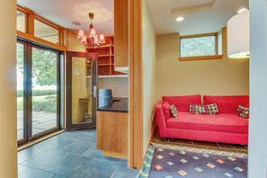 A modern interior with a red sofa, a kitchen area, and a large sliding glass door leading to an outdoor space. - Spacious 3BR Oceanfront - Chef's Kitchen (Anacortes)