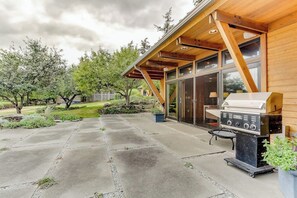 A covered outdoor patio with a barbecue grill, a stone-tiled floor, and a wooden pergola structure. - Spacious 3BR Oceanfront - Chef's Kitchen (Anacortes)
