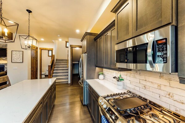 A modern kitchen with a central island, stainless steel appliances, and a staircase leading to another level. - Spacious 4BR Waterview Suncadia Resort (Cle Elum)