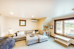A modern living room with a sectional sofa, a bench, a small table with a lamp, and a window with a view of the outside. - Spacious 4BR Waterview Suncadia Resort (Cle Elum)