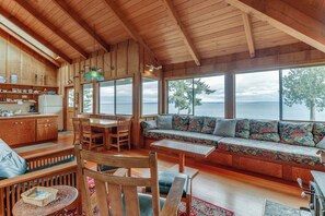 A wooden interior with a dining area, seating, and a view of the water. - 1BR water-view cabin with fireplace (Port Ludlow)