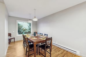 A dining area with a wooden table and chairs, a window with a view of trees, and pendant lights.