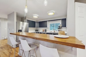 A modern kitchen with a wooden island, white bar stools, stainless steel appliances, and pendant lighting.