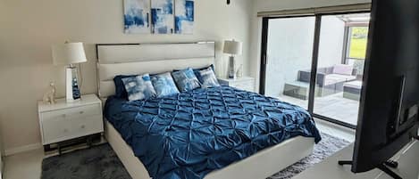 A bedroom with a large bed, two bedside tables with lamps, a ceiling fan, and a TV.