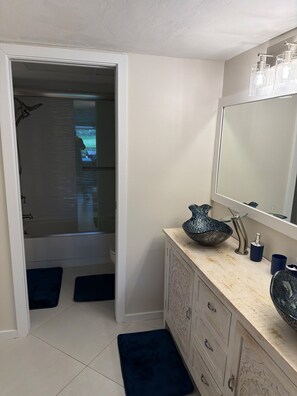 Een badkamer met een douche, een wastafel met glazen wastafel en een spiegel.