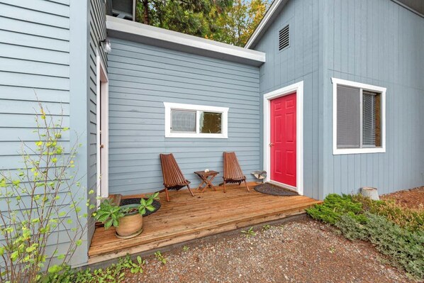 Une maison avec une terrasse en bois, une porte rouge et deux fenêtres.
