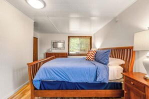 Une chambre à coucher avec un lit en bois, une table de chevet, une lampe et une fenêtre avec des stores.