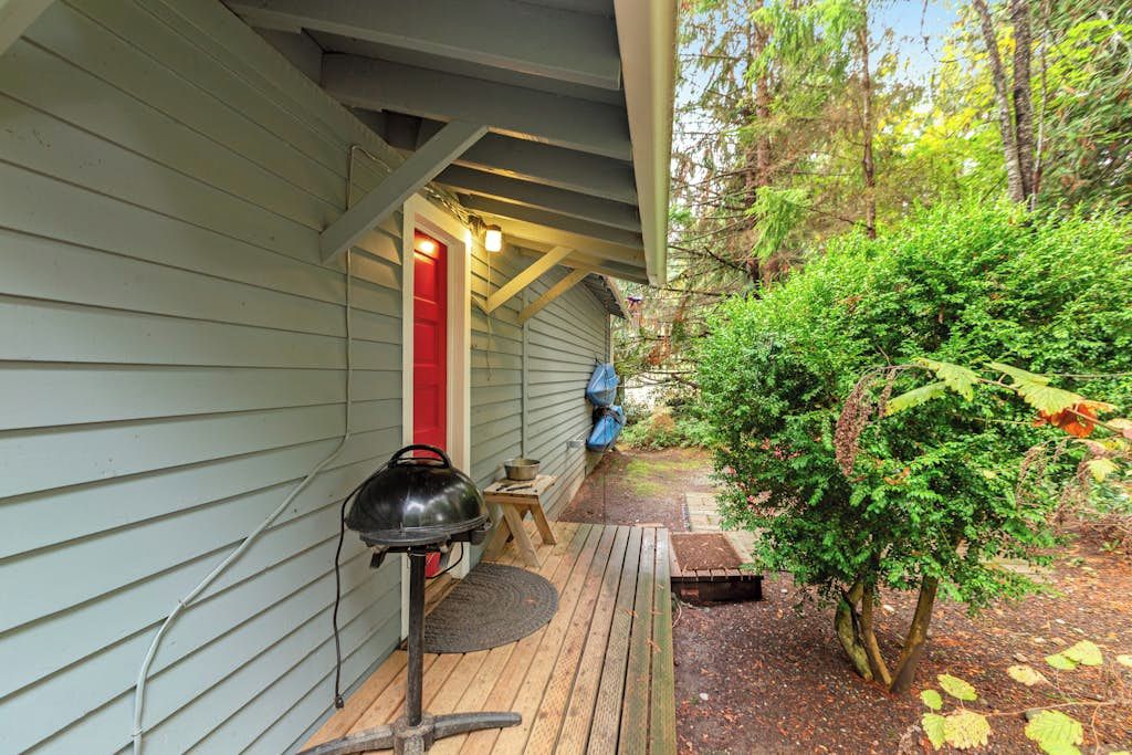 Une véranda couverte avec un barbecue, une porte rouge et une terrasse en bois.