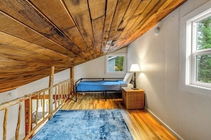 Ein Schlafzimmer mit schrägem Dach, einem Bett, einem Nachttisch und einem Fenster.