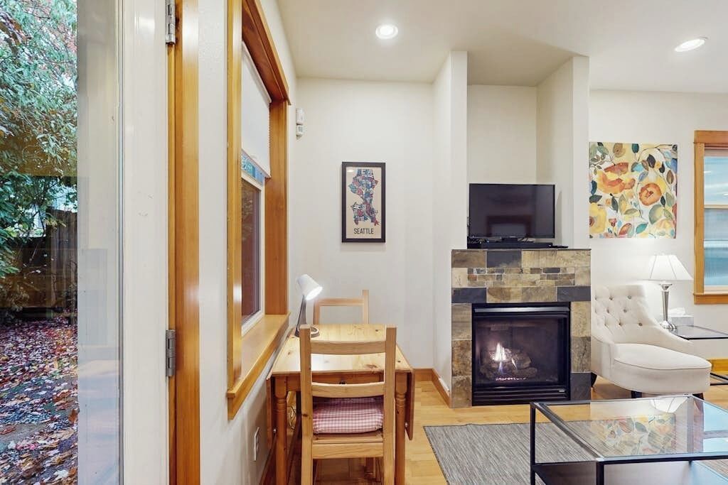 Een woonkamer met een open haard, een televisie en een eethoek met een tafel en stoelen.