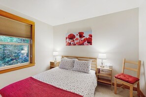 A bedroom with a bed, bedside tables, a chair, a window with blinds, and a wall-mounted artwork. - 2 BR townhome with gas fireplace and backyard (Seattle)