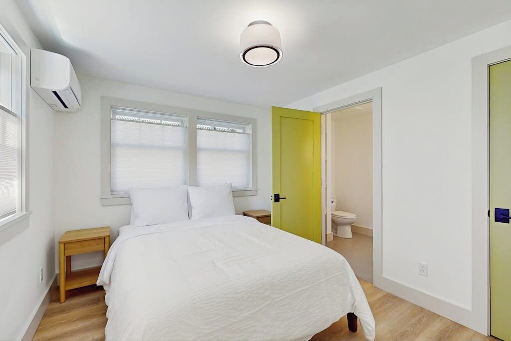 Ein Schlafzimmer mit Bett, Nachttisch, Jalousien und einer Tür zum Badezimmer.