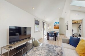 A modern living room with a flat-screen TV, a dining area with chairs, and a sofa with cushions. - 2BR Sun-Drenched Guesthouse - Cruise (Seattle)