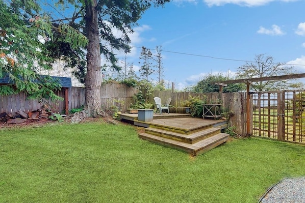 Un patio trasero con una terraza de madera, una silla y un portón.