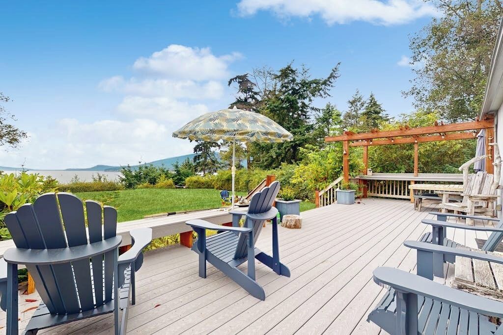 An outdoor deck with Adirondack chairs, a table, and an umbrella.