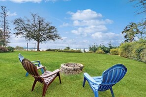 A grassy outdoor area with two Adirondack chairs, a stone fire pit, and a large tree. - 2BR family friendly getaway with deck and bay view (Anacortes)
