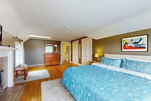 A bedroom with a large bed, a dresser, a nightstand, a painting, and a fireplace. - Charming, dog-friendly 3BR with terrace (Seattle)