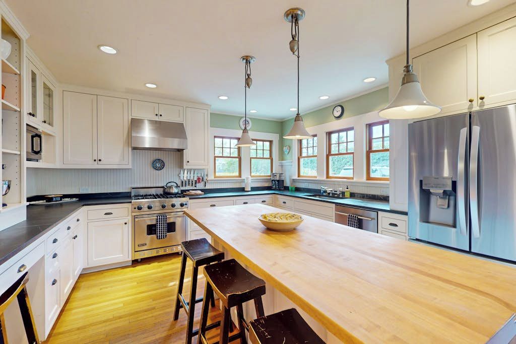 A modern kitchen with white cabinetry, stainless steel appliances, and a wooden island with bar stools.