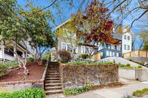 A residential area with a house featuring a front yard with a staircase leading to the entrance, a stone wall with climbing plants, and a neighboring house with a balcony. - Charming, dog-friendly 3BR with terrace (Seattle)