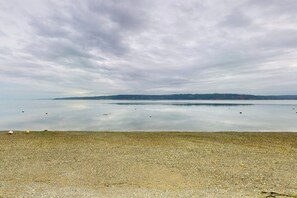 A pebbled beach with calm water and a distant shoreline.