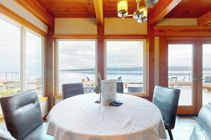 A dining area with a round table, chairs, and a view of the sea through large windows.