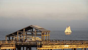 A pier with a skeletal structure and a sailboat in the distance.