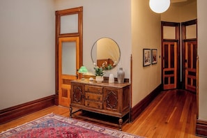 A hallway with a wooden floor, a large mirror, a wooden cabinet, and a patterned rug. - Historic Waterfront Hotel & Event Space and Kitchen (Port Townsend)