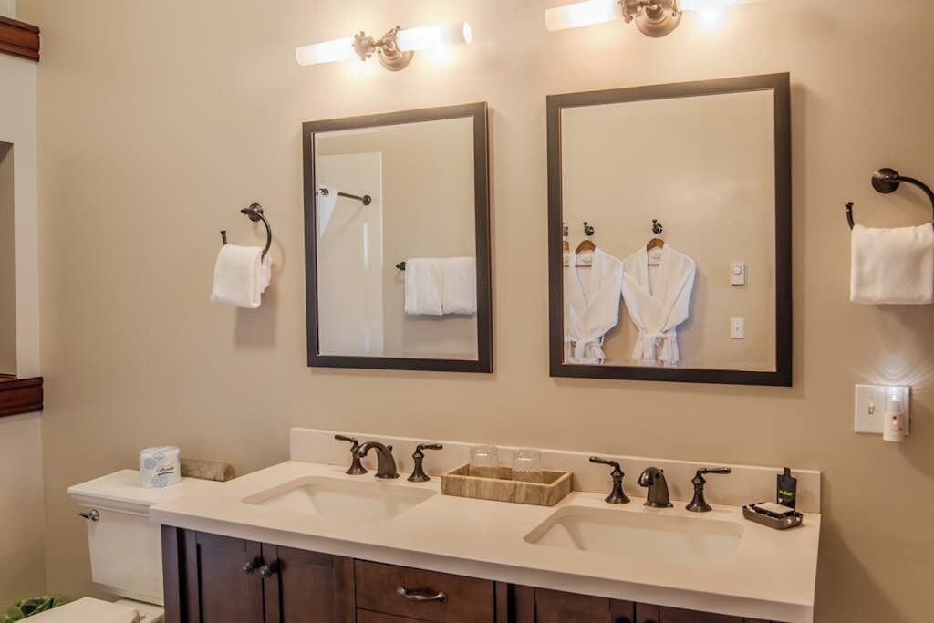 A bathroom with two mirrors, a sink with multiple faucets, and a toilet.
