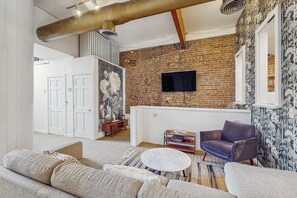 Ein Wohnzimmer mit Backsteinwand, Flachbildfernseher, Sofa, Couchtisch und einem gemusterten Teppich.