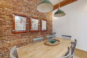 Ein Essbereich mit Backsteinwand, gerahmten Pflanzenbildern, einem Holztisch und Metallstühlen.