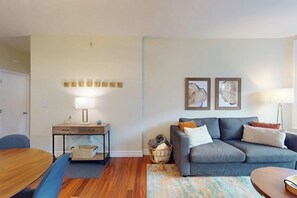 Ein Wohnzimmer mit grauem Sofa, einem Holztisch, einem Schreibtisch mit Lampe und einem Teppich.