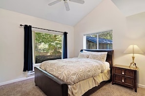 A bedroom with a bed, a nightstand, a lamp, and two windows.