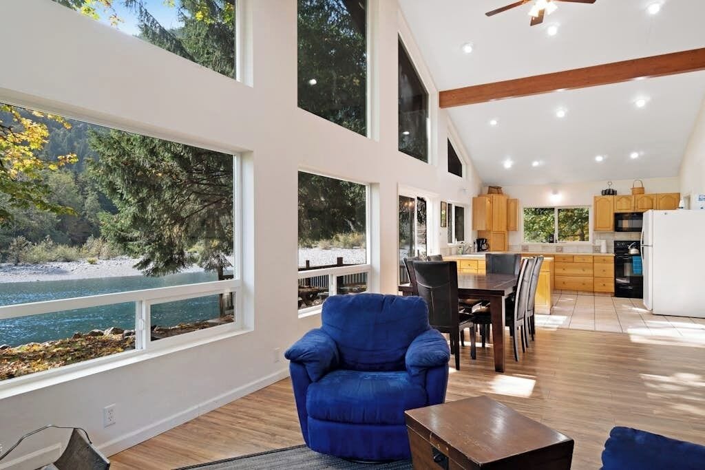 Amplia sala de estar con un ventanal grande con vistas a un lago, un comedor con mobiliario de madera y una cocina con electrodomésticos modernos.