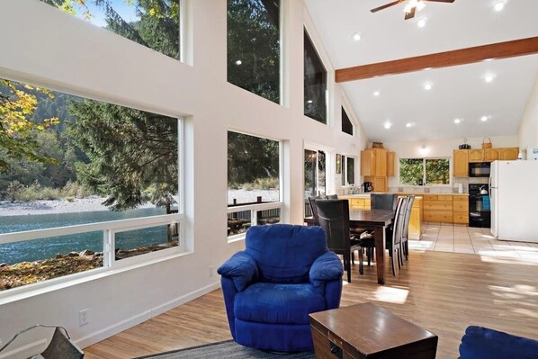 A spacious living area with a large window overlooking a lake, a dining area with wooden furniture, and a kitchen with modern appliances.