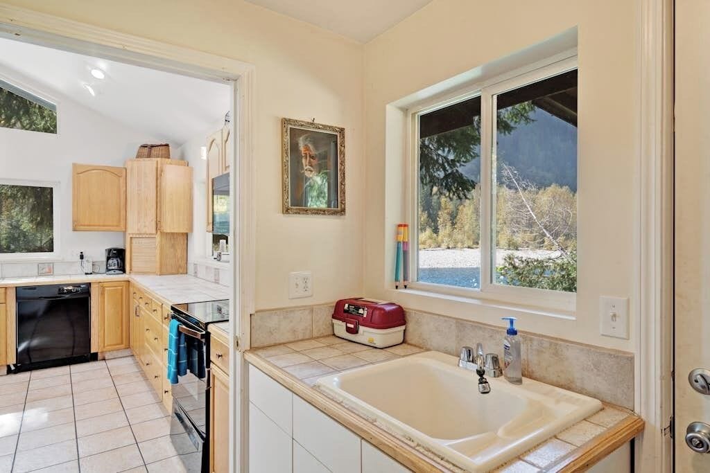 A kitchen with wooden cabinets, a dishwasher, and a window with a view of trees.